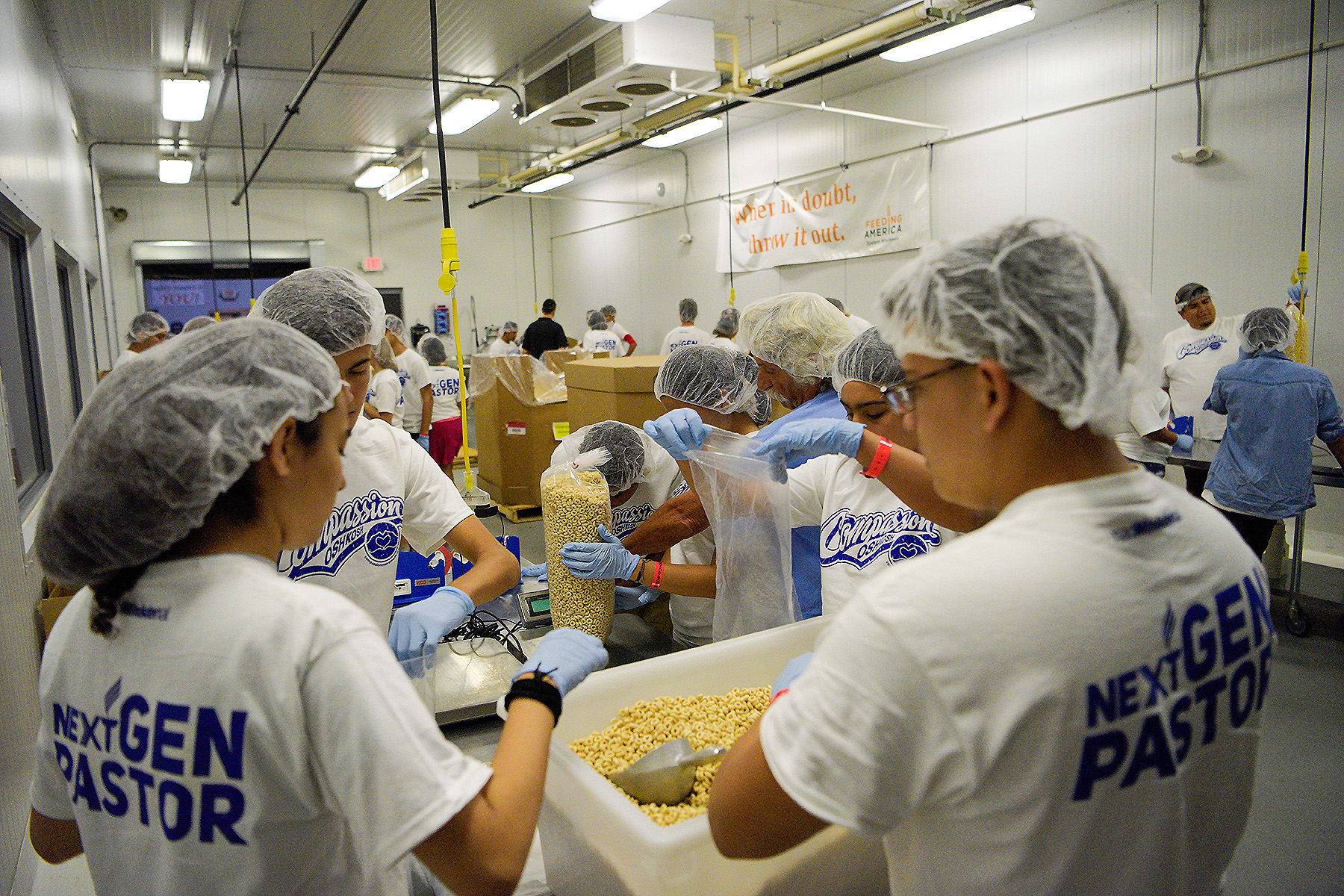 A group of young people wearing hair nets packing food in a warehouse for community service. 