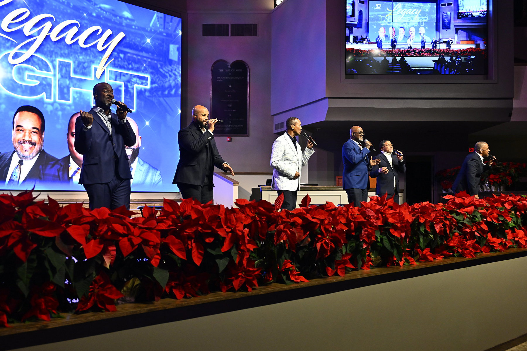 Six black men singing on a stage in front of a big screen reading "Legacy Night"